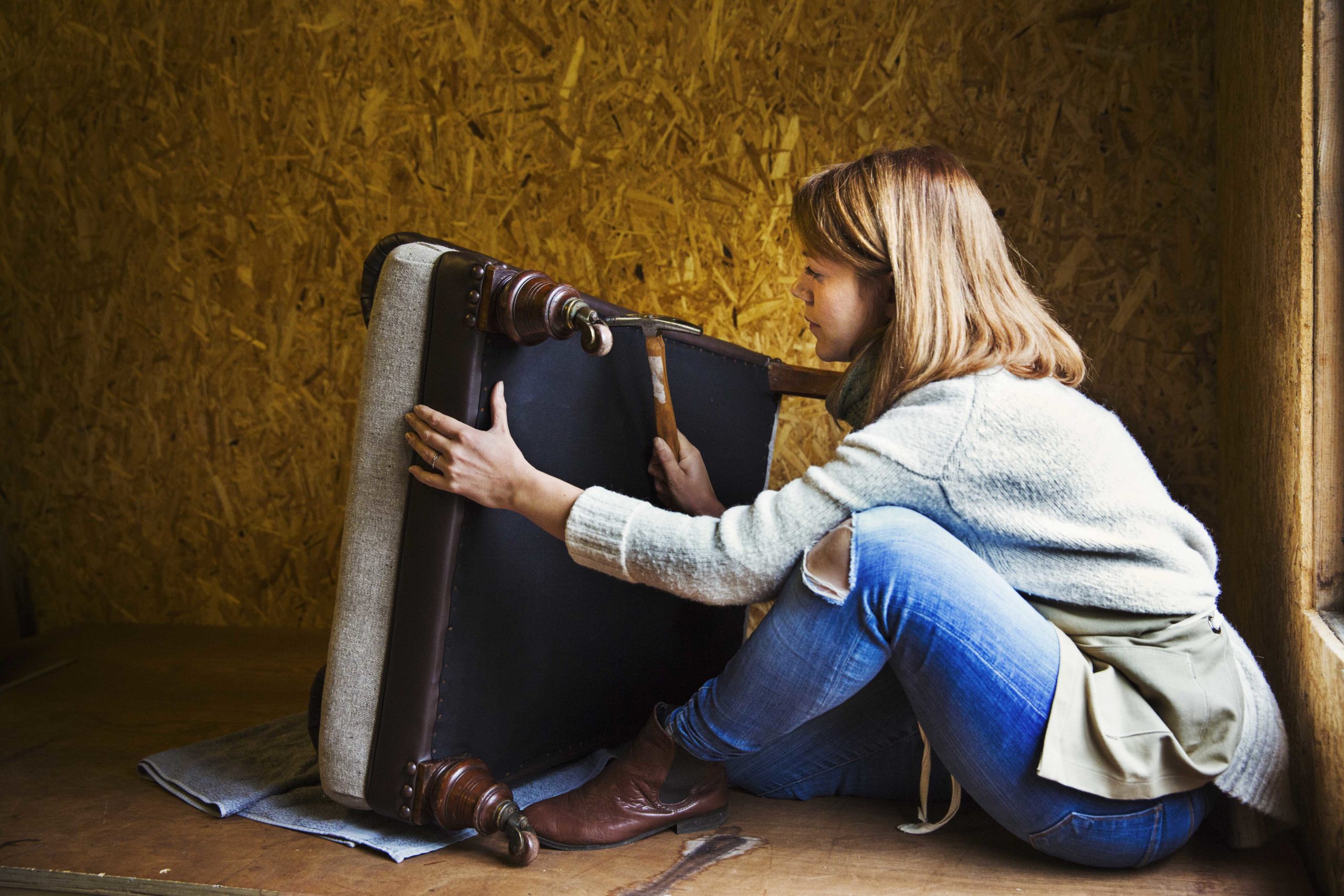 Upholstery workshop. An upholsterer working on the underside of a chair seat. ,Watlington ,England
